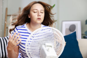 Young woman trying to cool off in front of an electric fan at home